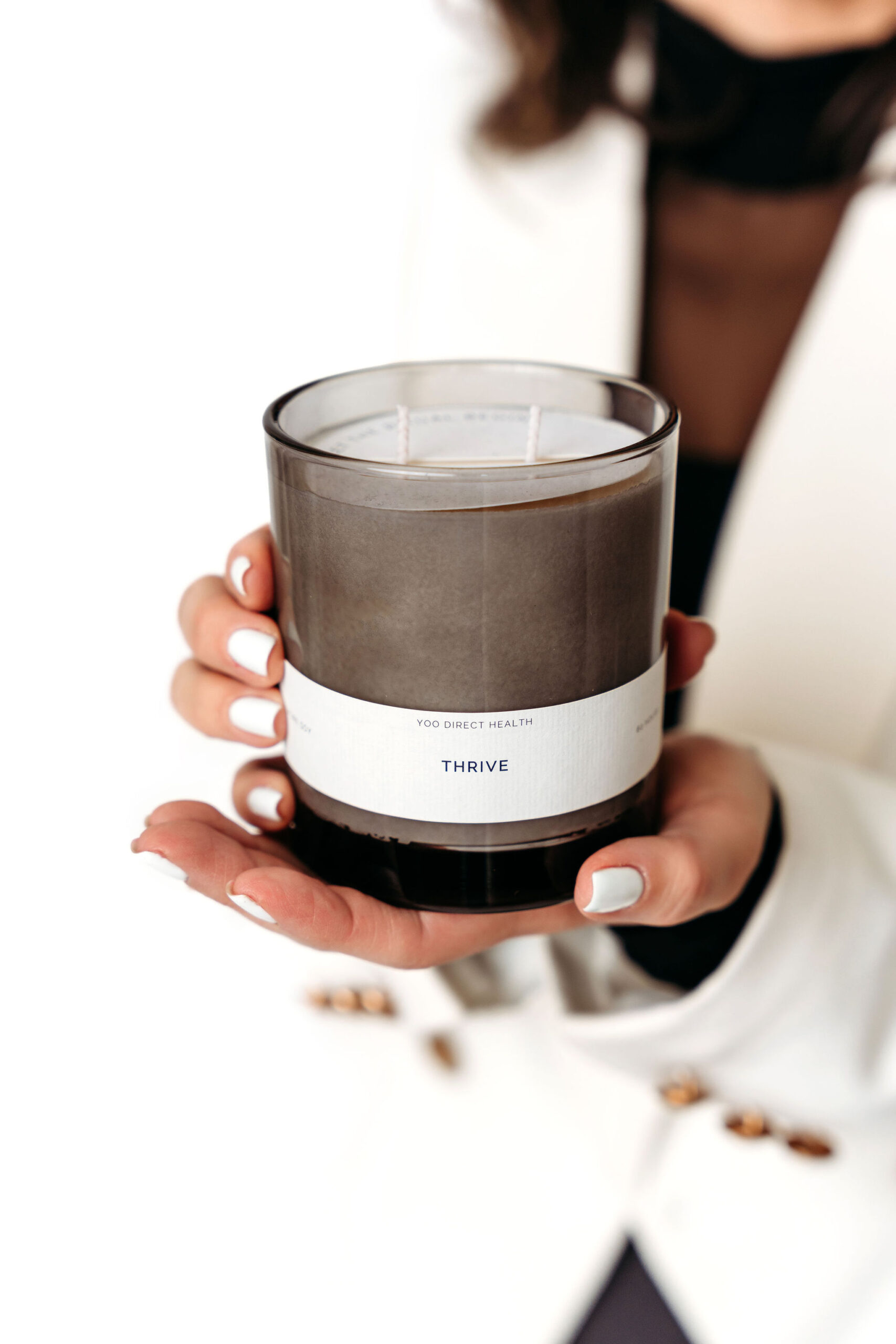Hands holding the Yoo Direct Health Thrive soy candle product