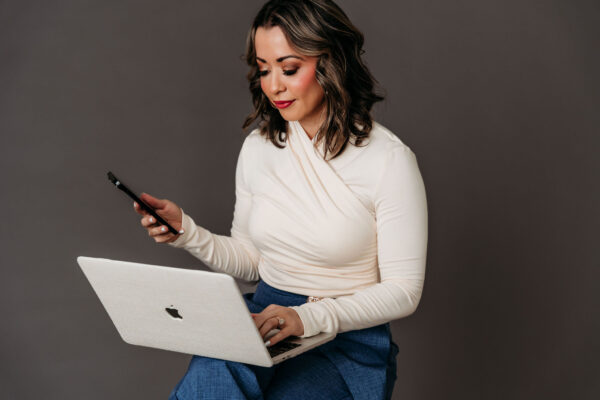 Lexi Yoo NP in a studio portrait reviewing content on her laptop and phone