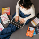 Lexi Yoo NP working on her laptop surrounded by reference books on menopause, peptides, and women's health