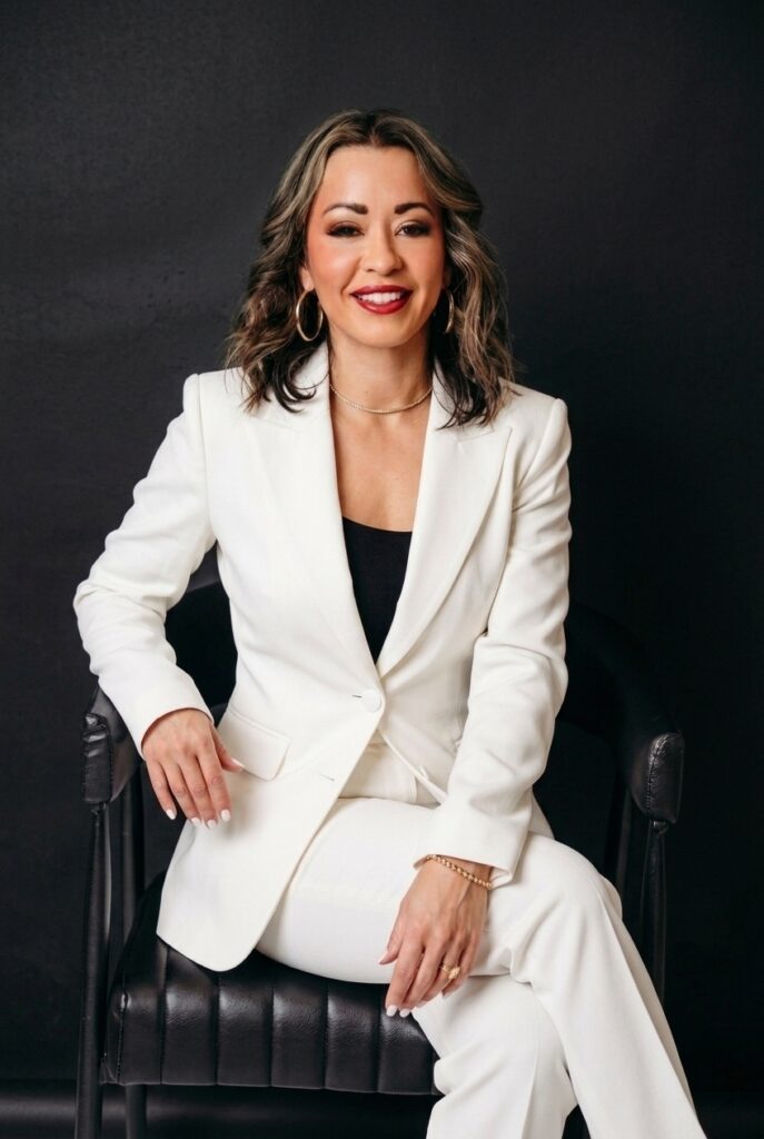 Lexi Yoo NP seated portrait in a white suit against a black backdrop