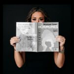 Lexi Yoo, nurse practitioner - Holding 'Manage Your Hormones' magazine over lower face, black top, dark background