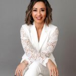 Lexi Yoo, nurse practitioner - White blazer with lace sleeves + white pants, seated on stool, grey background - general professional