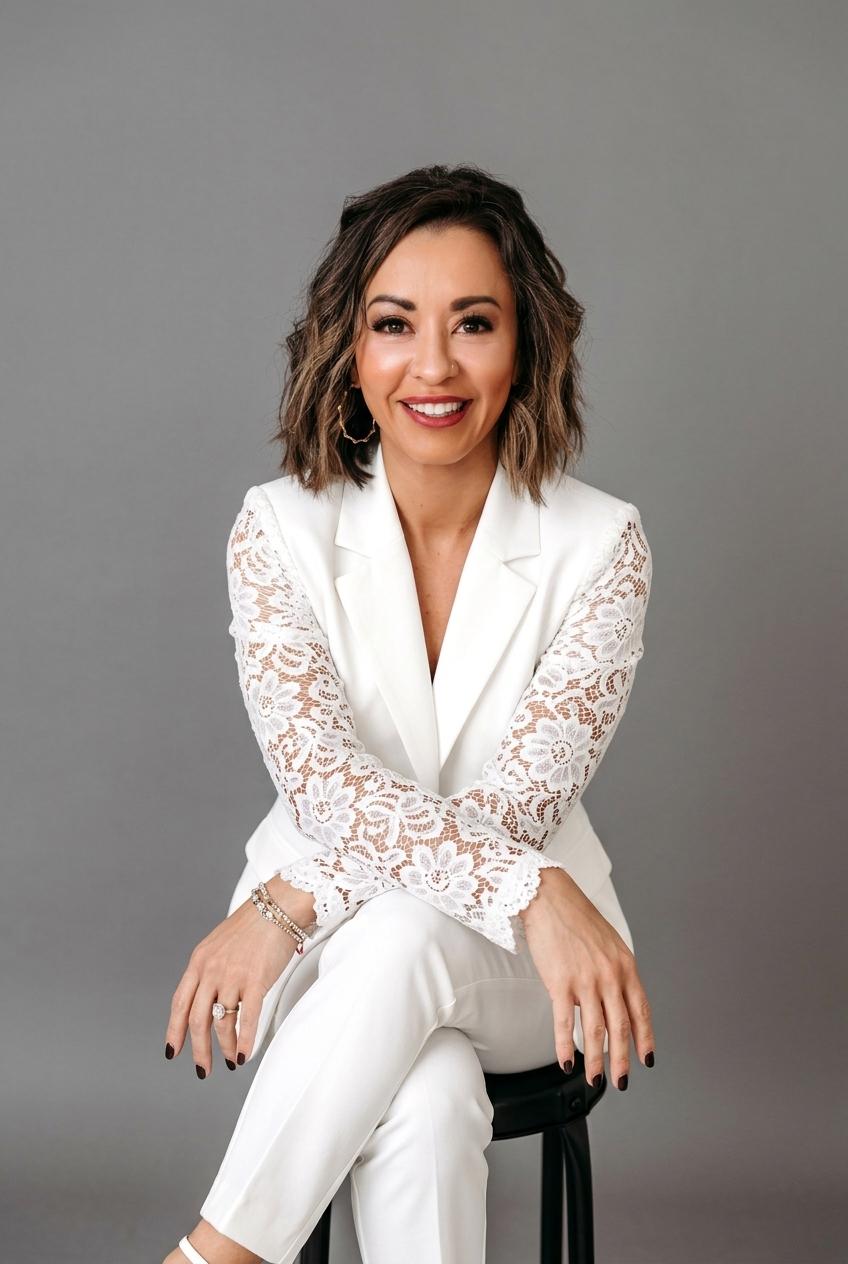 Lexi Yoo, nurse practitioner - White blazer with lace sleeves + white pants, seated on stool, grey background - general professional