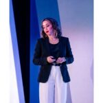 Lexi Yoo, nurse practitioner - On-stage keynote shot - black blazer + white pants, holding a presentation clicker, blue stage backdrop