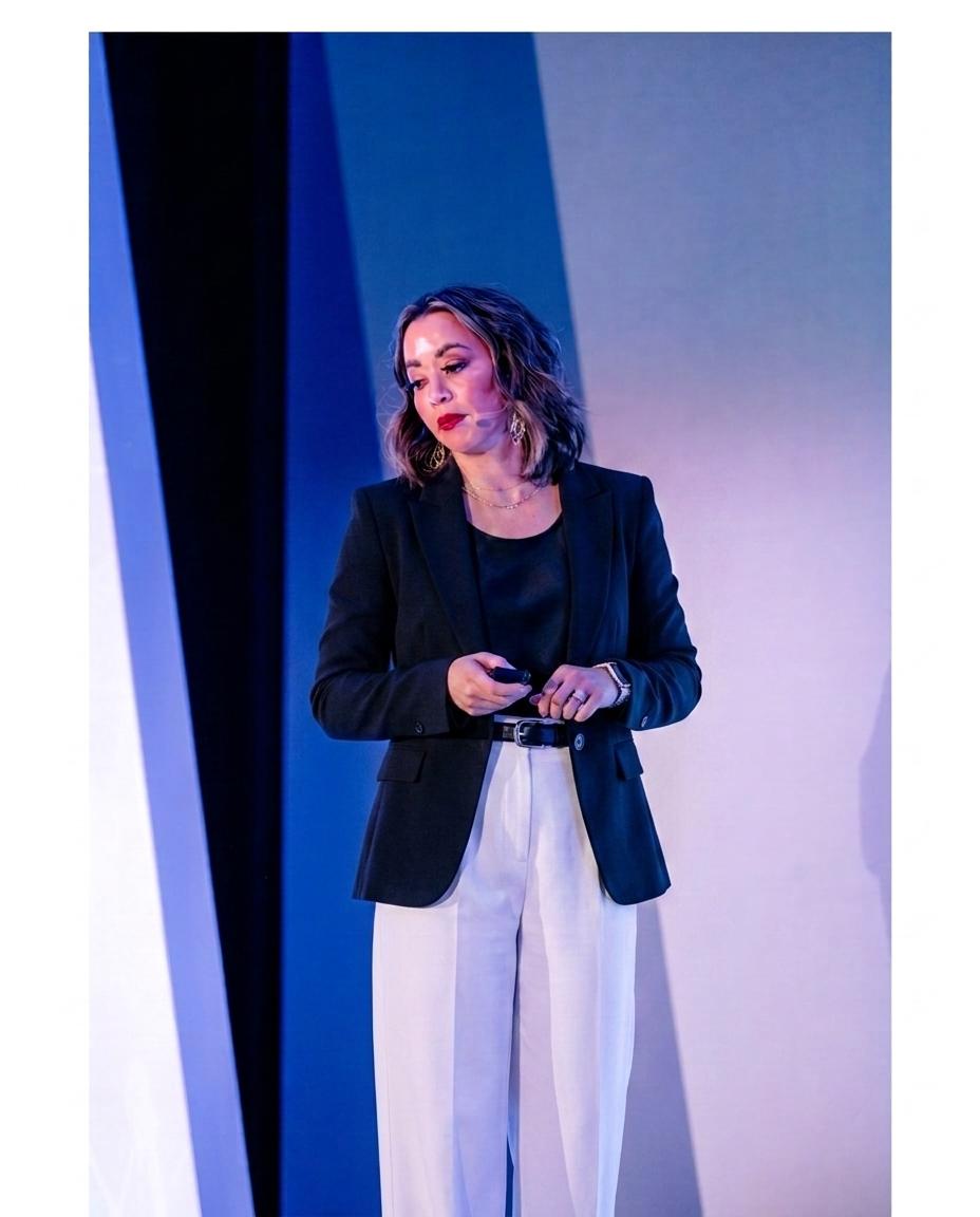 Lexi Yoo, nurse practitioner - On-stage keynote shot - black blazer + white pants, holding a presentation clicker, blue stage backdrop