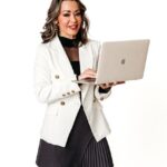 Lexi Yoo, nurse practitioner - White blazer + grey pleated skirt, holding open laptop, white background - general professional