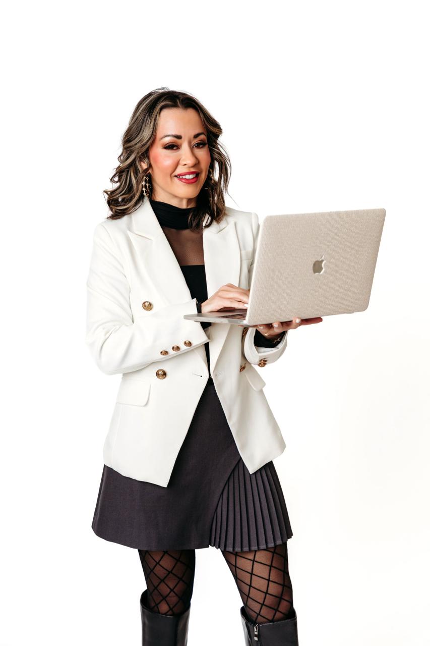 Lexi Yoo, nurse practitioner - White blazer + grey pleated skirt, holding open laptop, white background - general professional