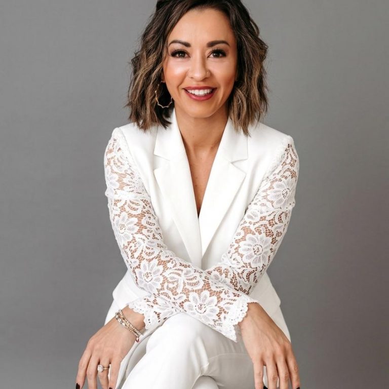Lexi Yoo, nurse practitioner - White blazer with lace sleeves + white pants, seated on stool, grey background - general professional