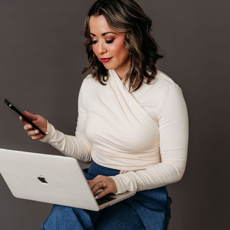 Lexi Yoo NP in a studio portrait reviewing content on her laptop and phone